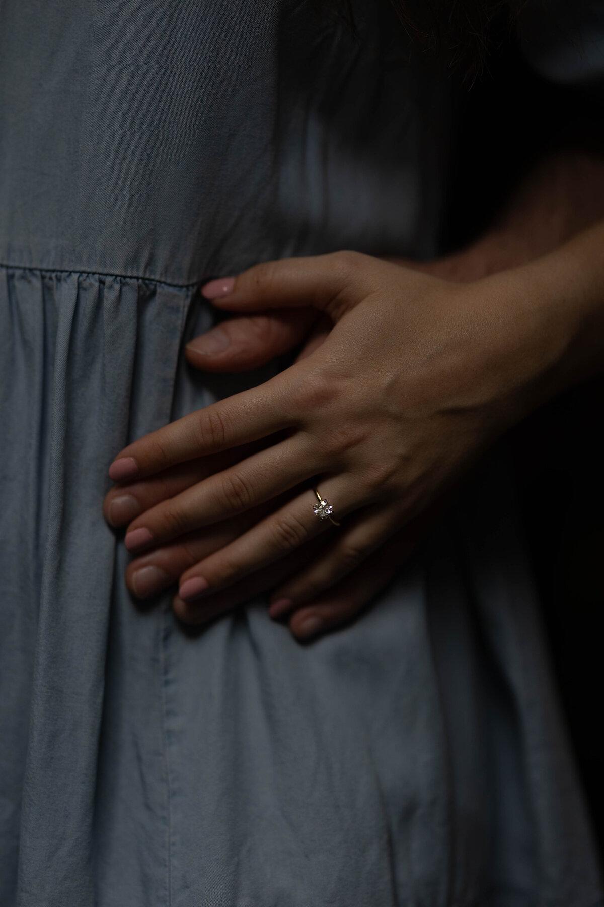 Hand resting on a partner's dress at the waist, engagement ring visible, intimate close frame